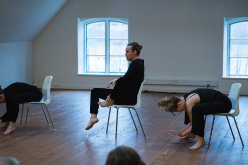 Voksne mennesker sidder på stole og strækker ud