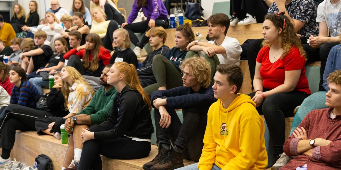 Unge mennesker sidder på en trappe og lytter til en der snakker